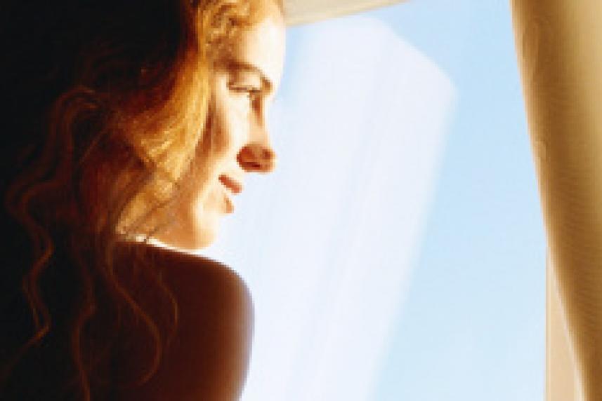 Photo: Young woman staring out a window during sunrise