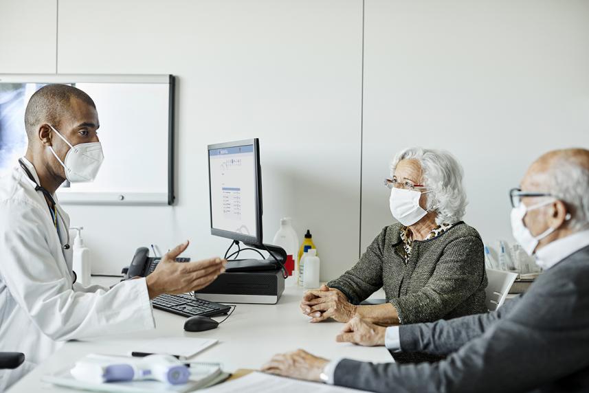 Doctor discussing with senior couple, all wearing masks