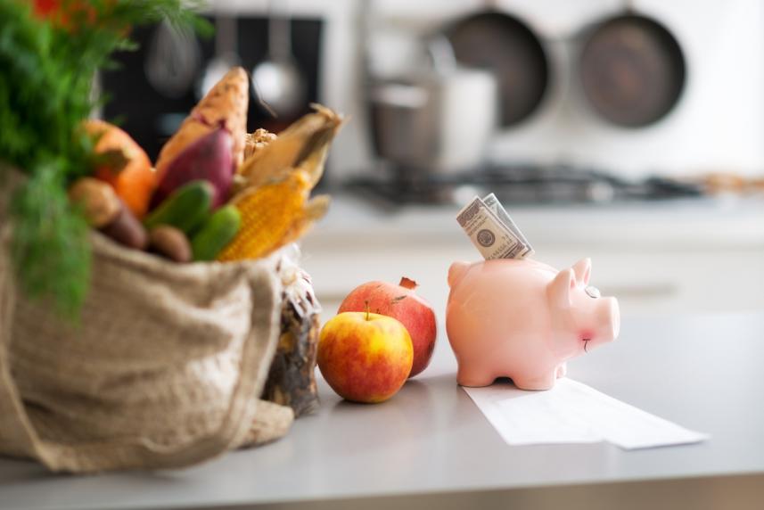 Photo: Piggy bank on kitchen counter next to a bag filled with fresh produce