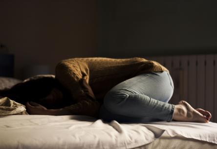 Depressed woman curled up on a bed