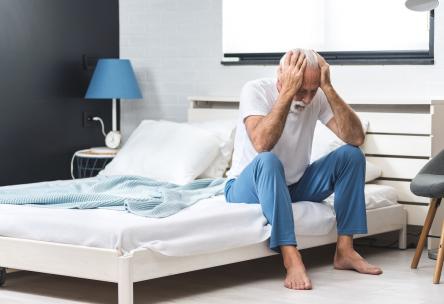 Depressed man sitting on bed with head in hands