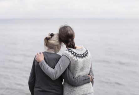 Mother and daughter embracing each other, looking at the ocean