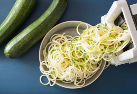 Zucchini being formed into pasta noodle-like strands (zoodles) with a spiralizer