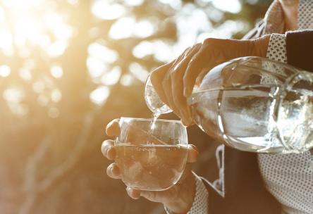 Hands of senior woman pouring glass of water by window - stock photo